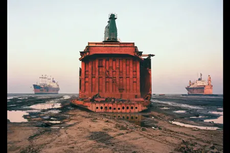 The carcass of a cargo ship, already sheared of its forward structure, sits where it was parked on the beach at Chittagong, Bangladesh, flanked by two other scrapped vessels in various states of dismemberment.
