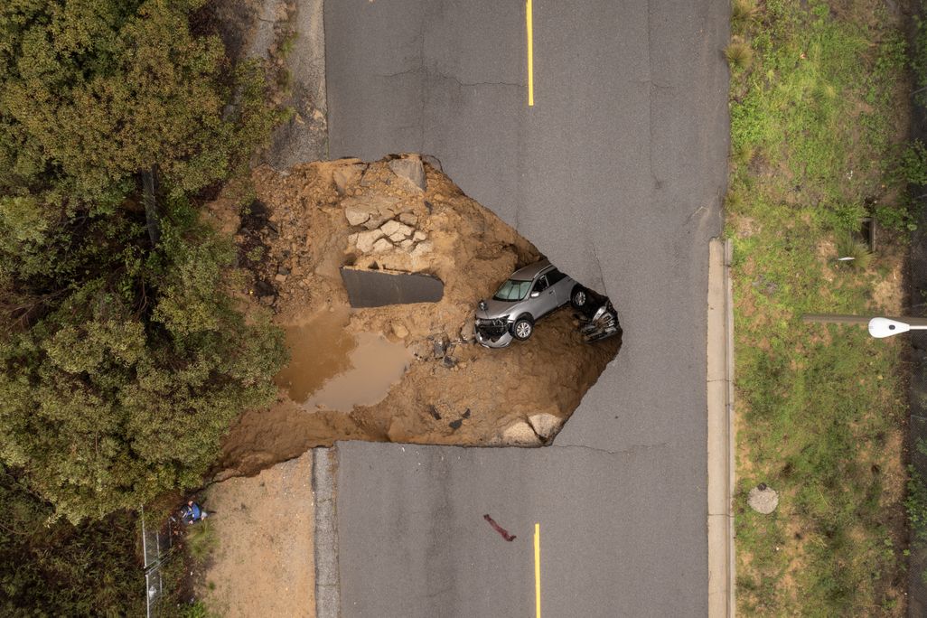 An aerial view of two cars lying in a sinkhole under a road.
