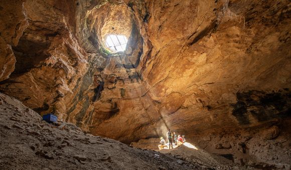 OPENER - A shaft of golden light from the cave’s mouth provides warmth as the expedition’s scientists enjoy lunch 80 feet below the opening of Natural Trap Cave.