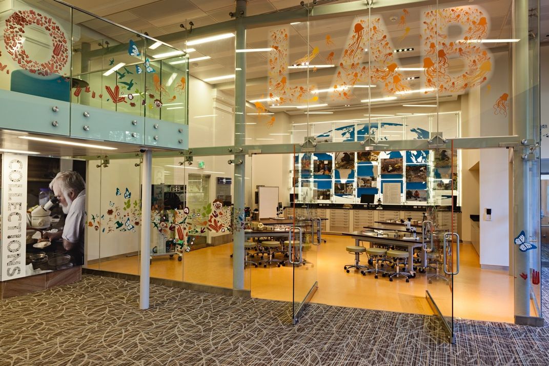 Doors open to glass enclosed room with empty tables and stools