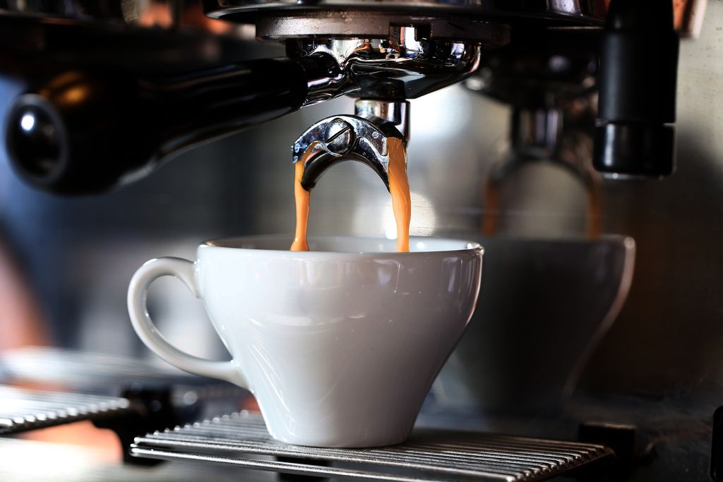 Coffee pouring into small white cup from espresso maker