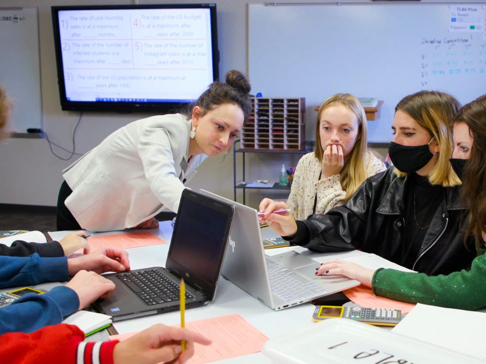 Peterson wears a bun and blazer pointing towards a computer screen with her students