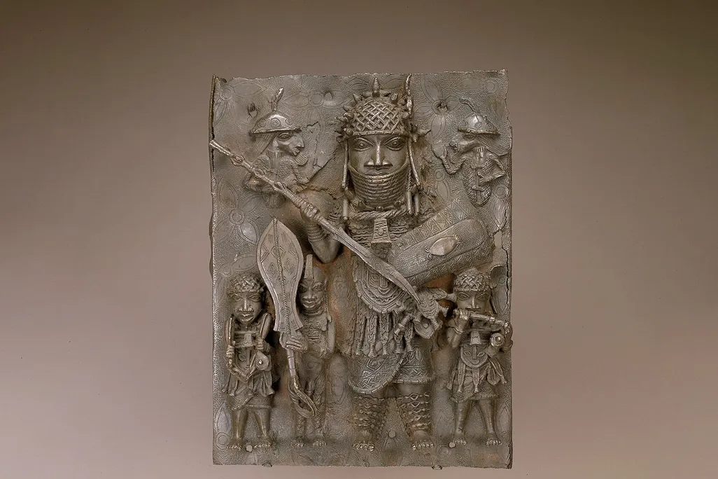 A view of a bronze plaque depicting an oba, or king, with a spear and sword standing over smaller figures beneath him