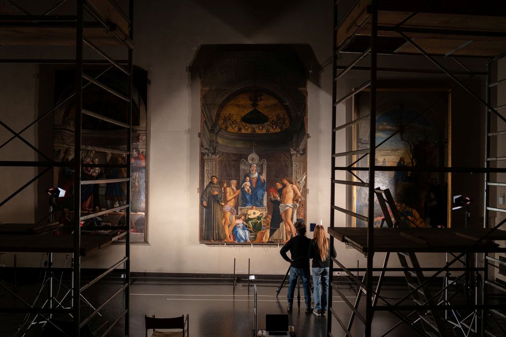 A painting on a wall with a bright light pointing at it and two people standing in front, surrounded by scaffolding
