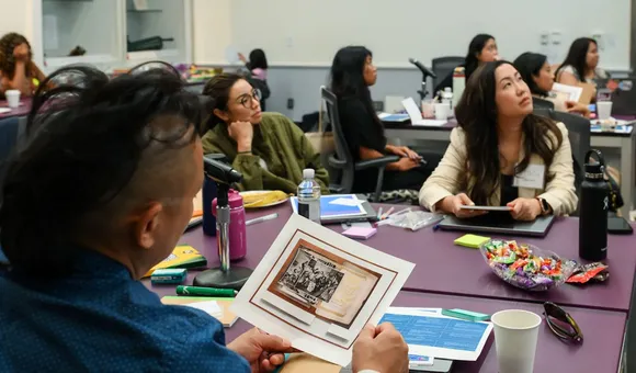A man in a blue shirt looks at a photograph of archival images while several other people look toward a presentation