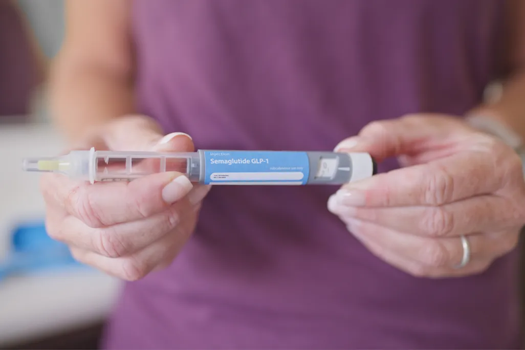 closeup of hands holding a GLP-1 injection pen that says "semaglutide"