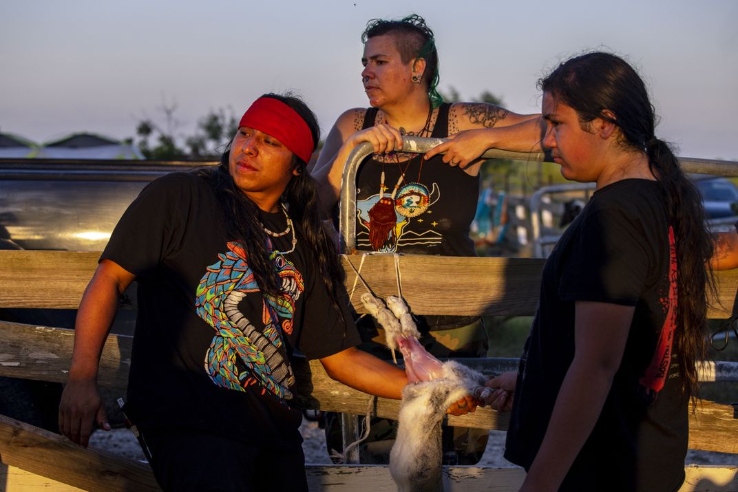 Three young people skin a rabbit in dim light