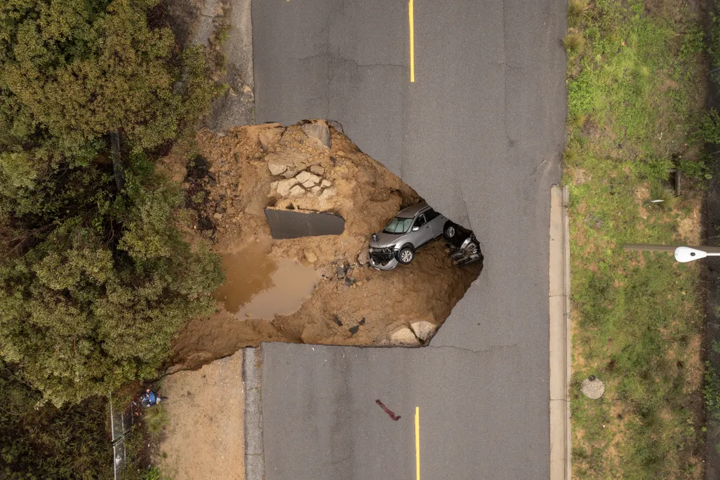An aerial view of two cars lying in a sinkhole under a road.