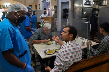 A customer talks to a waiter in a mask while eating his meal at a table divided with transparent panels in Bangalore, India.