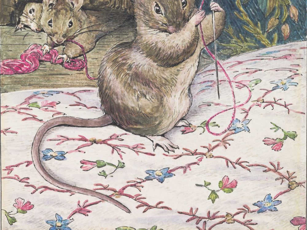 A brown mouse holds a needle and piece of pink thread and works on a delicate embroidery pattern of pink, blue and green flowers on white cloth, while two mice look on behind