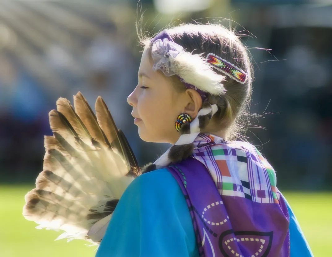a girl wears beads and feathers from her Native tribe