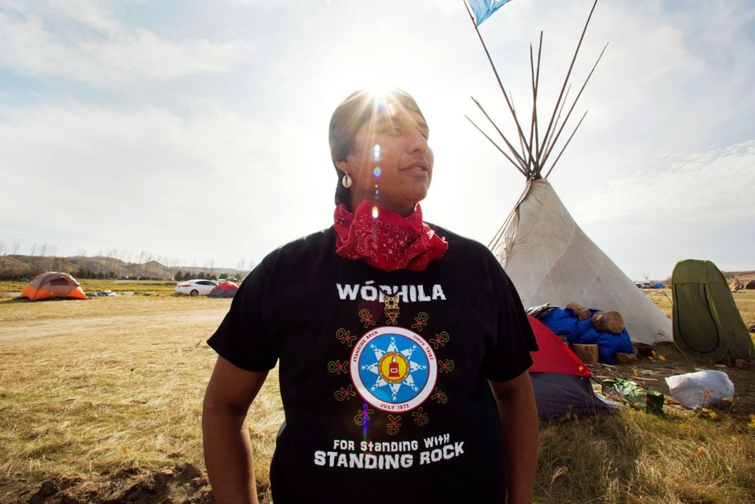 A native man stands in front a tipi tent