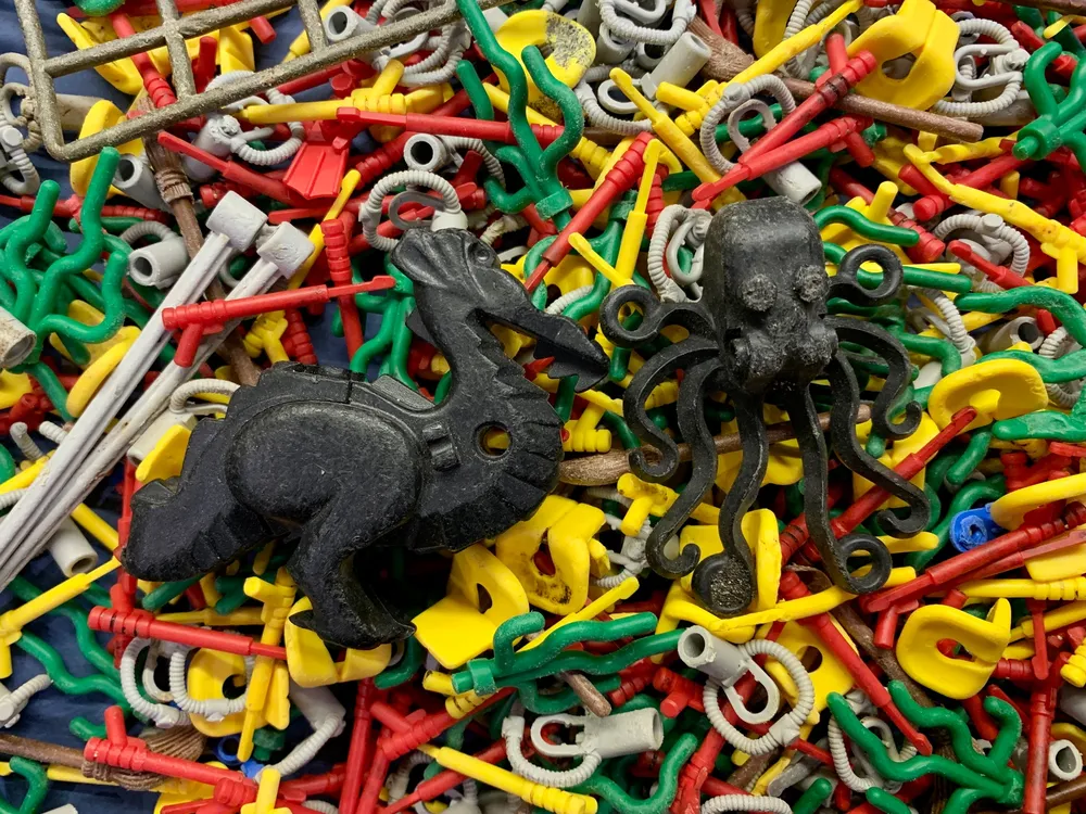 An image of random pieces of Legos that were recovered from beaches in England. In the image there is two large black lego pieces. One is an octopus and the other is a dragon.