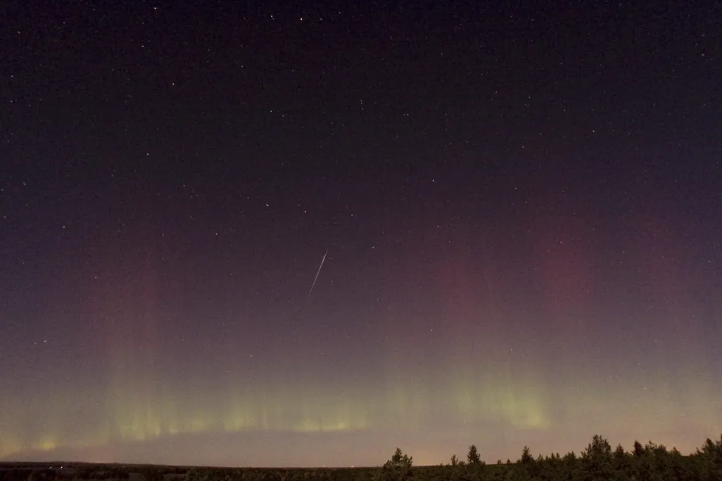 a draconid meteor streaks across the sky with the northern lights visible