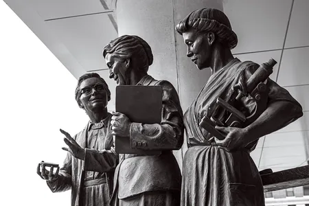 This seven-foot statue of Pearl Kendrick, center, and Grace Eldering, left, was unveiled in Grand Rapids in 2019. Lab assistant Loney Clinton stands to the right with a microscope.