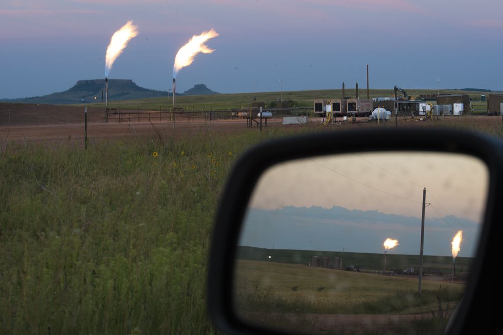 View of flaring at an oil well through a car window and through its side view mirror