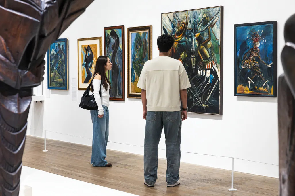 Two people look at a wall of paintings