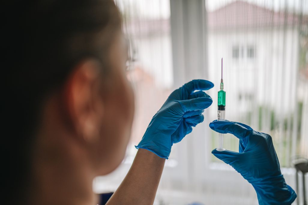An over-the-shoulder shot of a woman, wearing blue gloves, preparing a syringe.