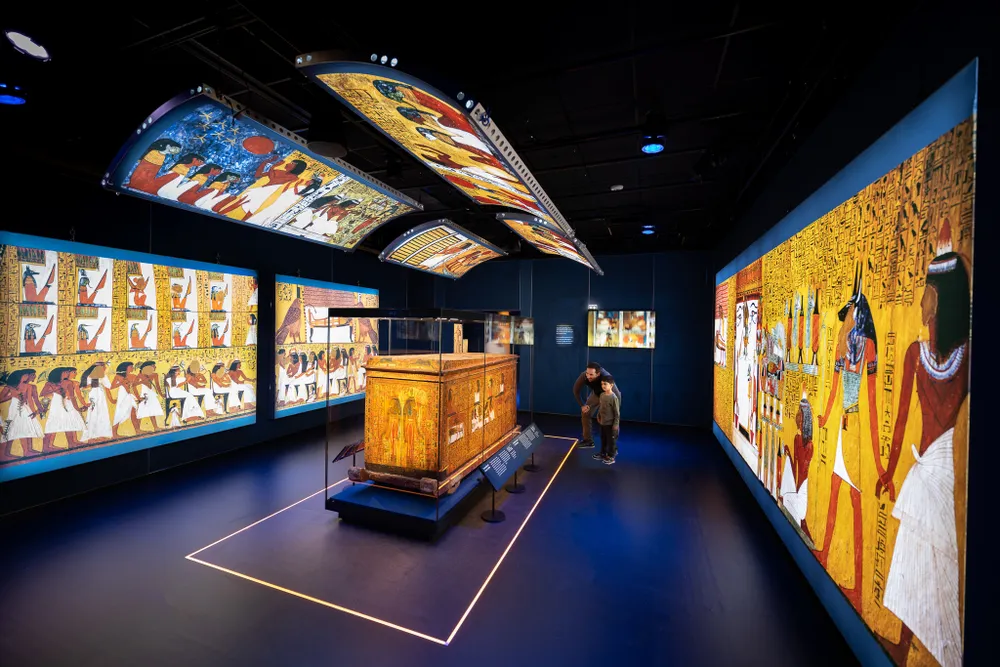View of the exhibition, featuring lighted displays on the walls and a coffin in the middle of the room