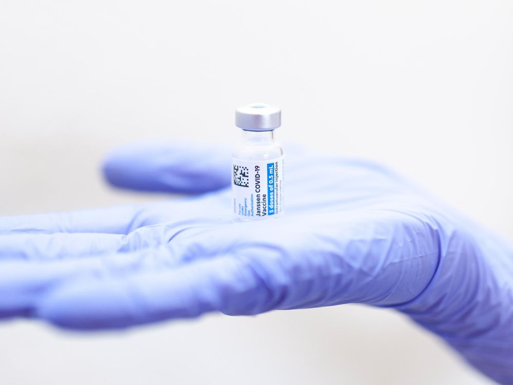 Blue gloved hand holds a small glass vial of Johnson and Johnson covid-19 vaccine