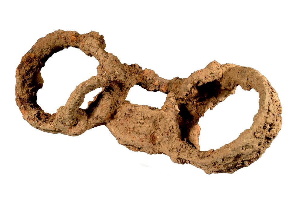 An image of a very rusted pair of shackles, two circles connected by a padlock that would have encircled someone's ankles