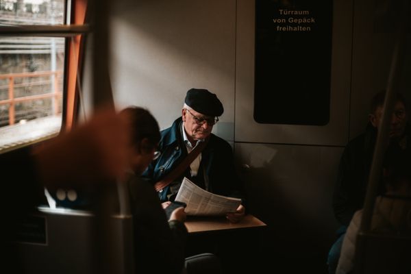 An old man sitting in a metro, reading a newspaper. thumbnail