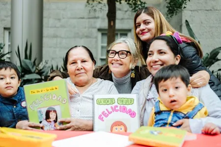 Woman smiles at the center of a group with young children and their mothers showcasing books they created