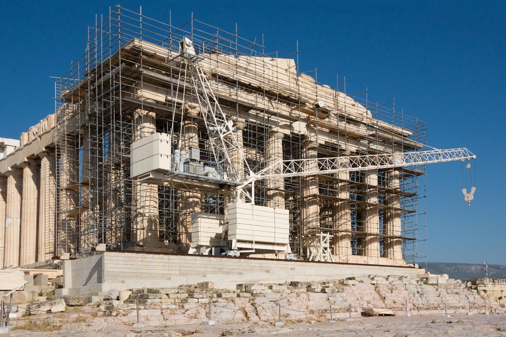 A view of the side of the Parthenon, on a sunny day with clear blue sky behind; the facade is covered in scaffolding and construction equipment