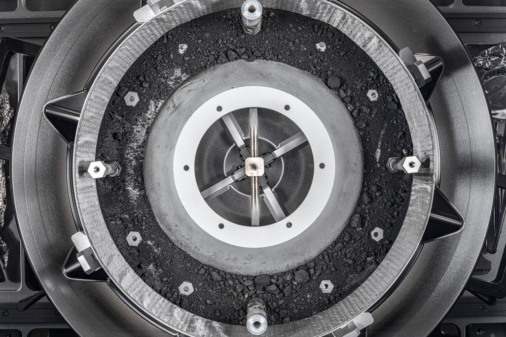 An aerial view of an open circular and grey canister with bits of dust and tiny rocks inside