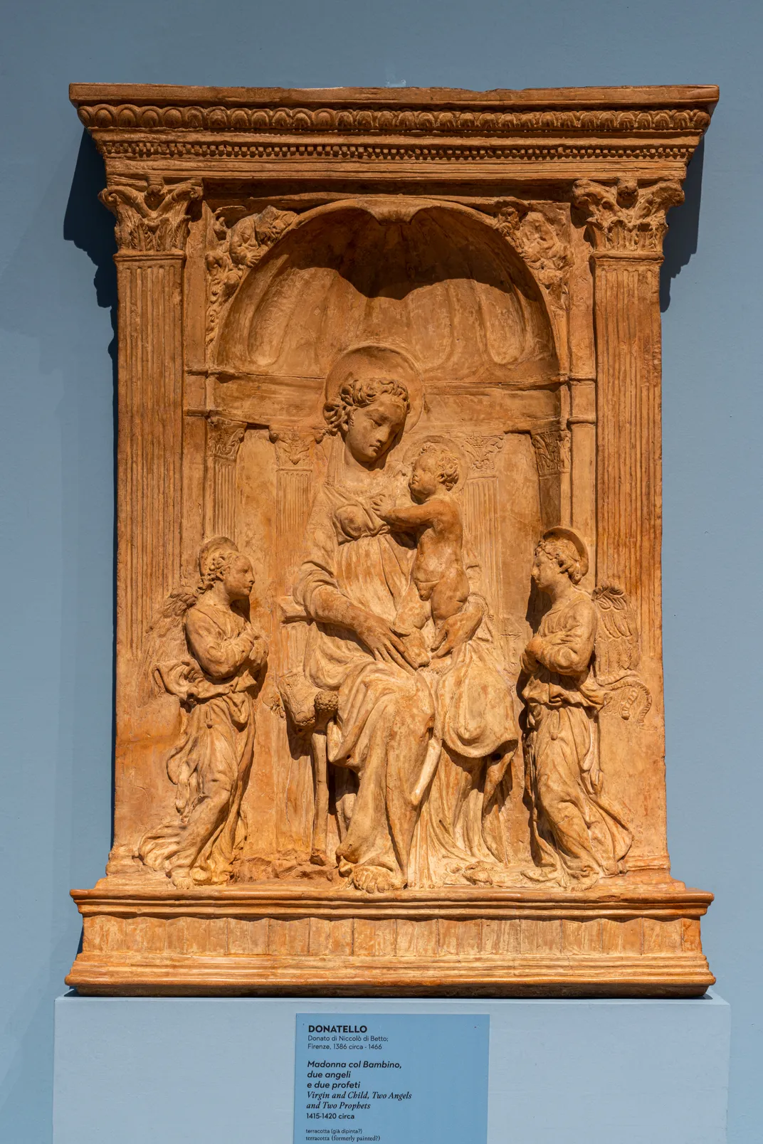 A sculpted relief made from reddish orange terracotta depicting the Virgin Mary seated with a baby Jesus in her lap