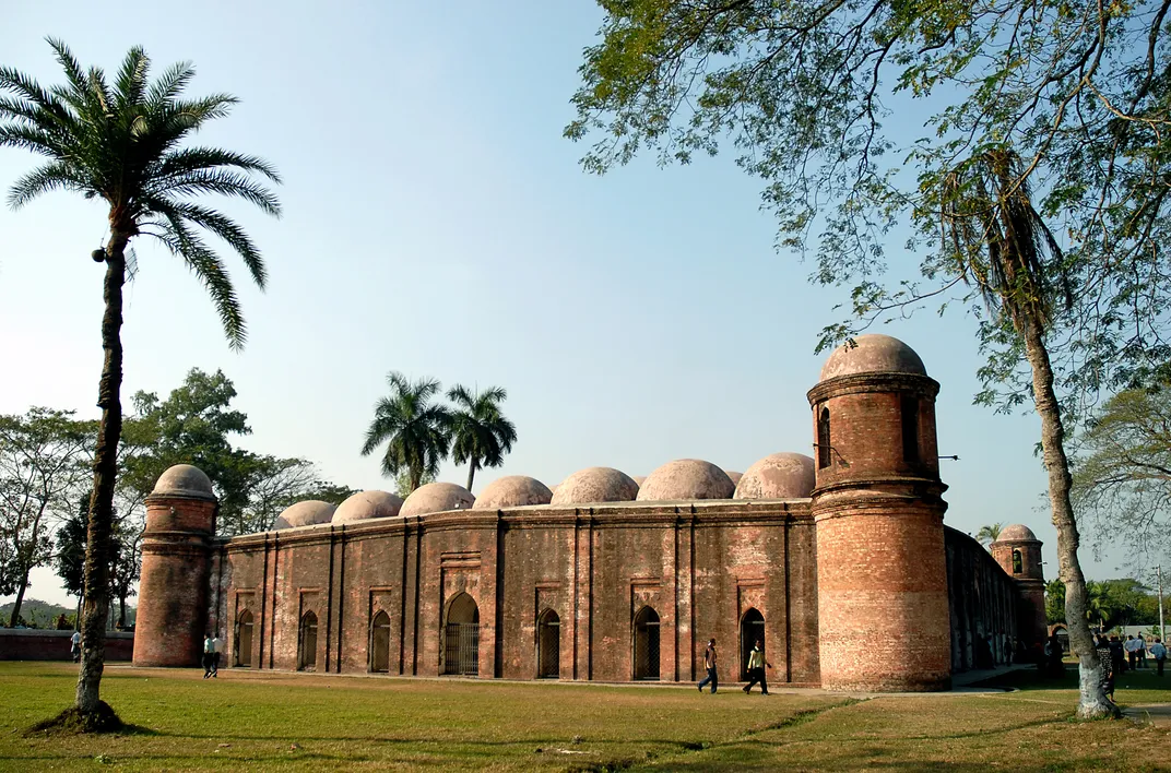 A reddish stone mosque surrounded by palm trees