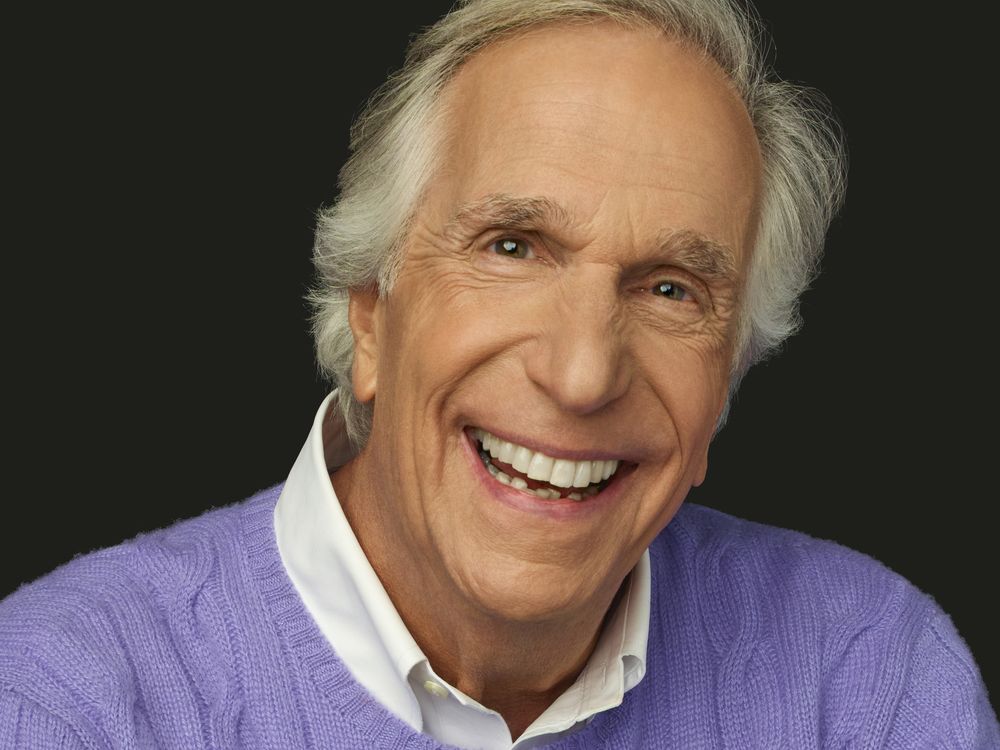A headshot of Henry Winkler, shows a close-up the actor looking directly into the camera, his eyes twinkling above a broad, white smile.