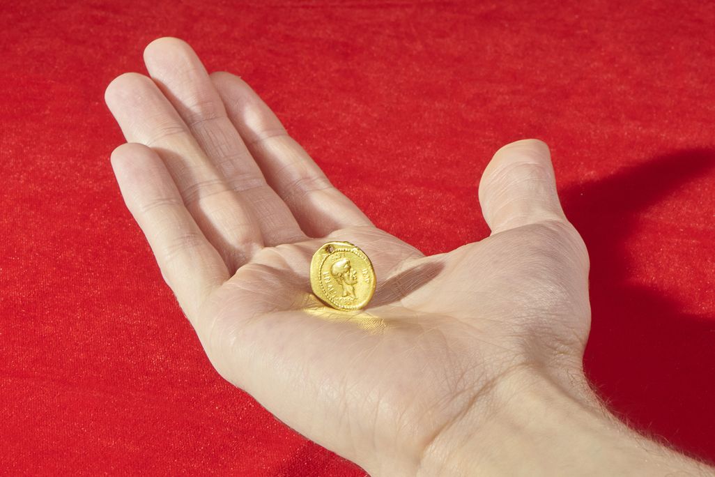 A white hand extends over a red background and holds the golden coin in their palm