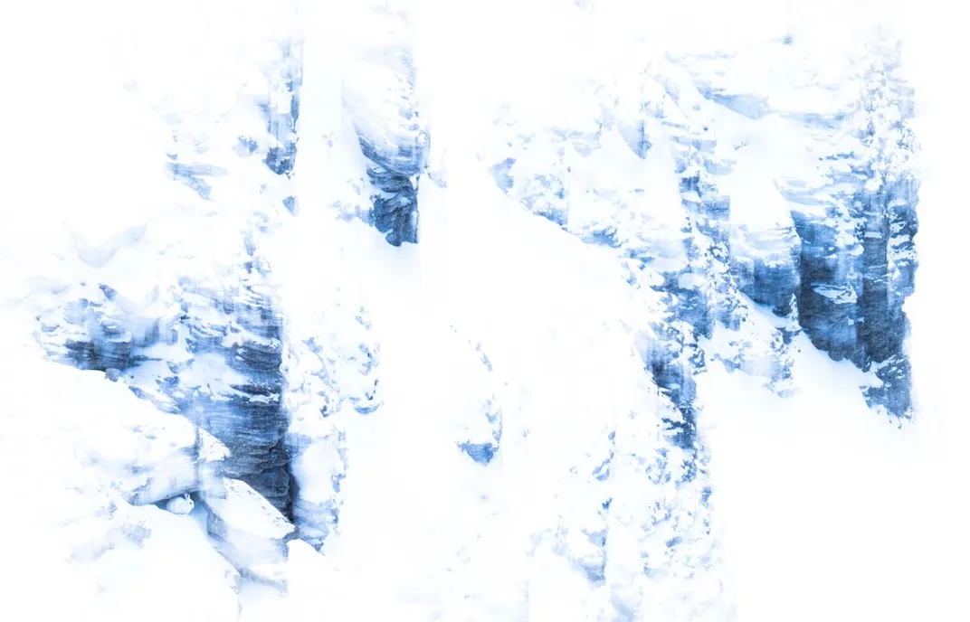amid a vast snowy landscape, a small, white hare sits in a rocky alcove, hard to see