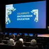 A woman stands at a podium in a theater with "Celebrate Smithsonian Education" projected on the screen