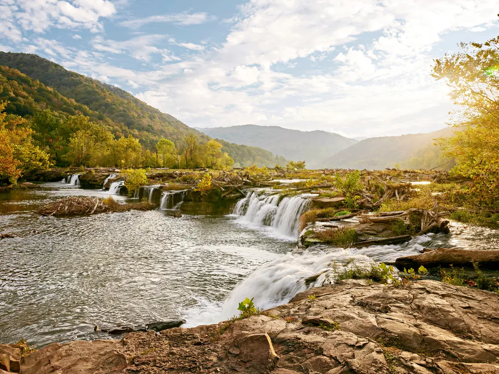 Sandstone Falls in New River Gorge National Park, with cascading water, rocky ledges, and fall foliage along the riverbanks.