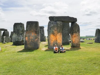 Just Stop Oil protesters&nbsp;Rajan Naidu, 73, and Niamh Lynch, 21, sit in front of Stonehenge after covering the monument in orange powder.
