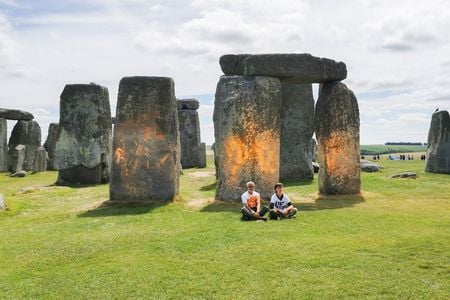 Just Stop Oil protesters&nbsp;Rajan Naidu, 73, and Niamh Lynch, 21, sit in front of Stonehenge after covering the monument in orange powder.