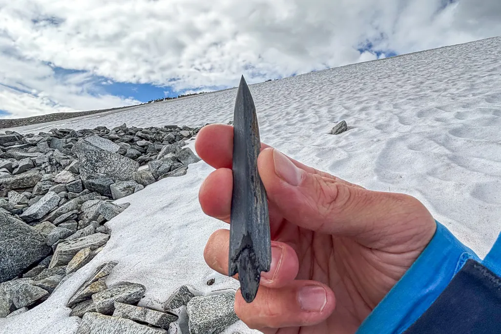 A person's hand holding up an arrowhead with snow in the background