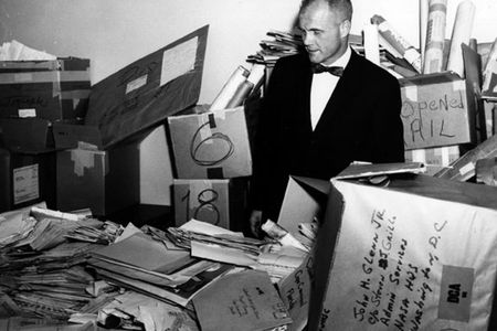 John Glenn stands in the NASA mailroom surrounded by thousands of letters sent to him.