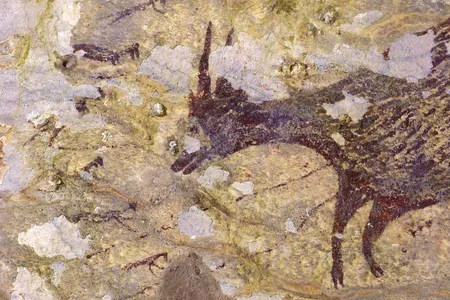 Six humanoid figures with animal features surround an anoa, a small type of buffalo, in a 44,000-year-old Indonesian cave mural.