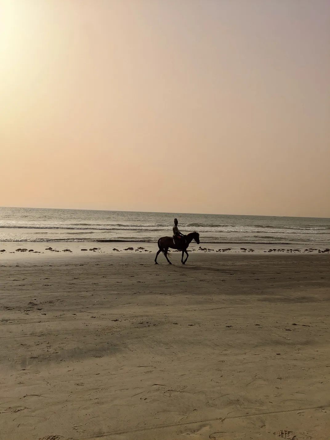 An African man rides a horse on a empty beach