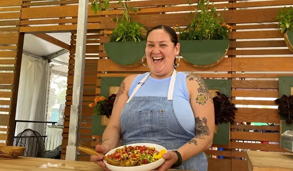 Candid photo of Elena Terry smiling holding a white dish full of colorful beans, peppers, and corn tilted away from her.