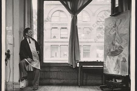 Yasuo Kuniyoshi, in his New York City Studio in 1940, is at work on the painting Upside Down Table and Mask, currently on view at the Smithsonian American Art Museum.