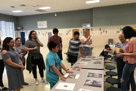 Group of adults and middle school children standing and actively discussing a set pf printed pictures laid out on a central table.