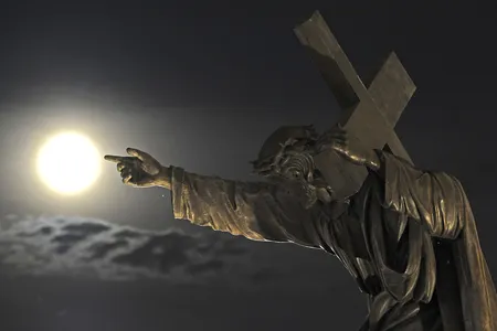 A statue in front of the Holy Cross church in Warsaw, Poland, guides viewers toward the August 2014 supermoon.