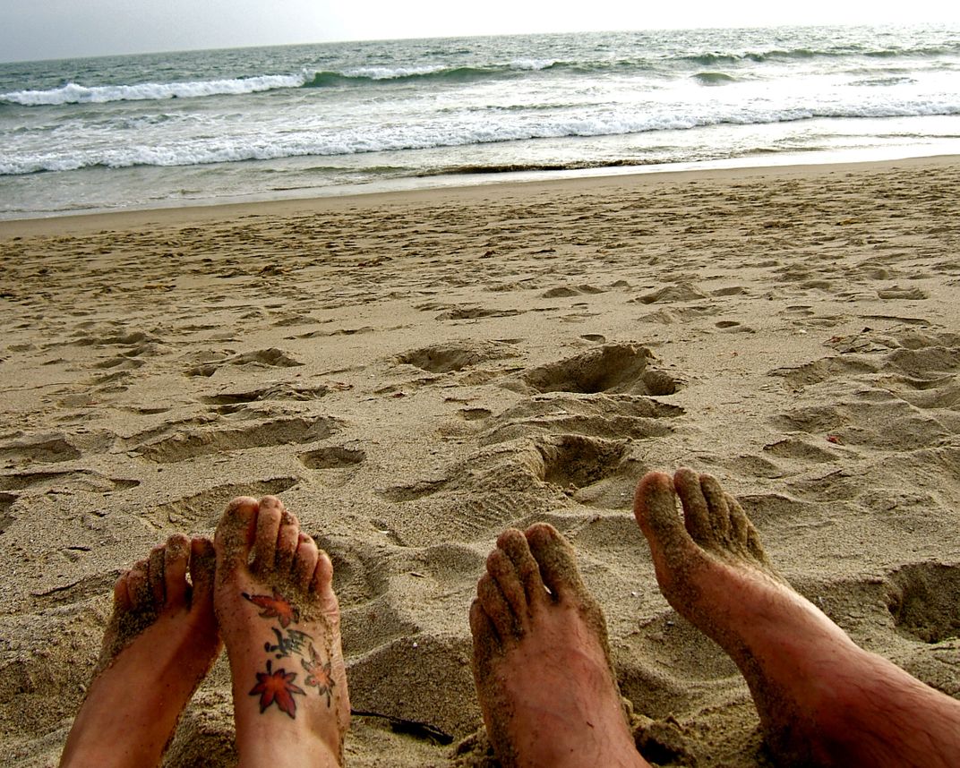 Two people's feet on the beach next to the ocean