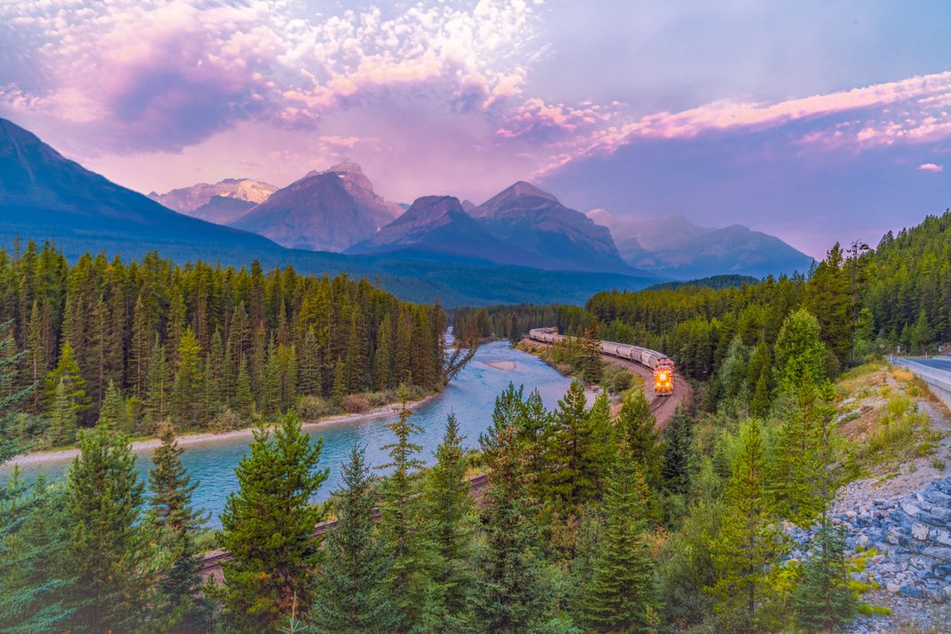 A train winds along a river in the Canadian Rockies.