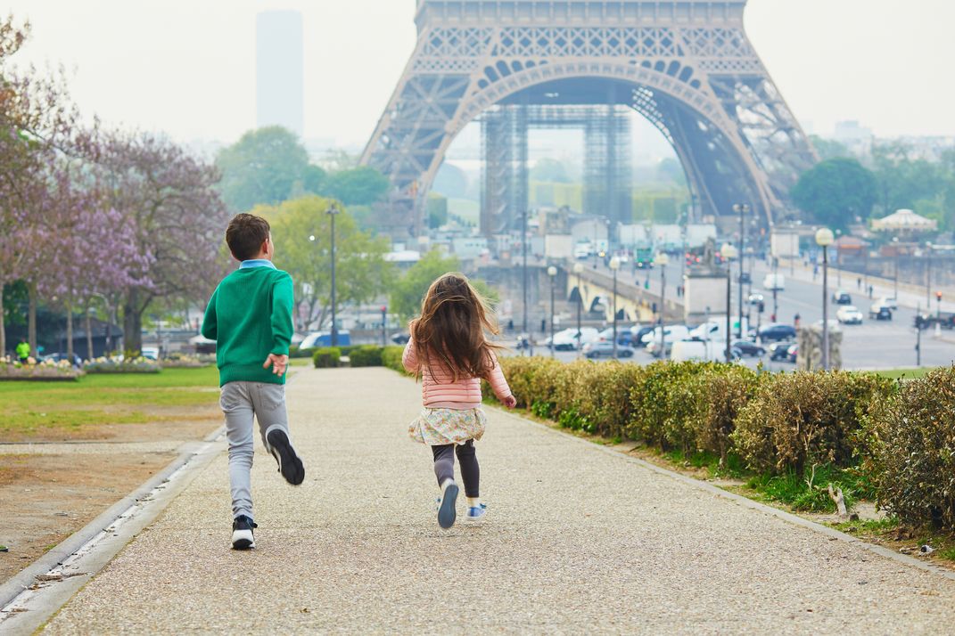 Kids run in a park next to the Eiffel Tower
