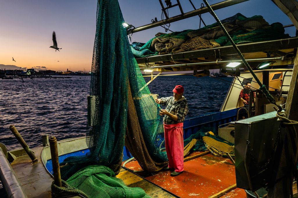 Fisherman fixing a net on a boat at dusk